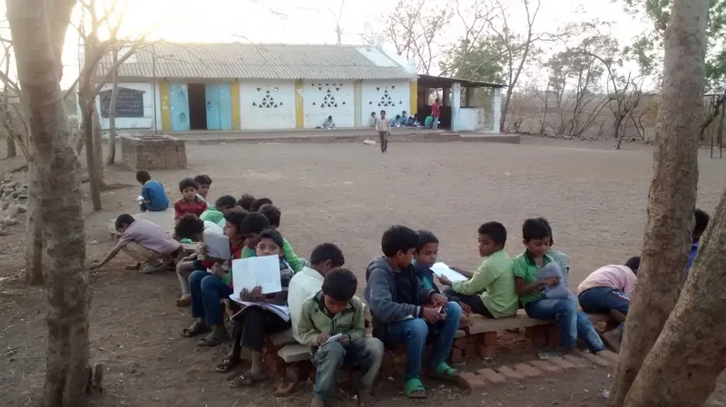 आधारशिला के खुले परिसर में छोटे समूहों में किताब-कॉपी पढ़ते बच्चे।
